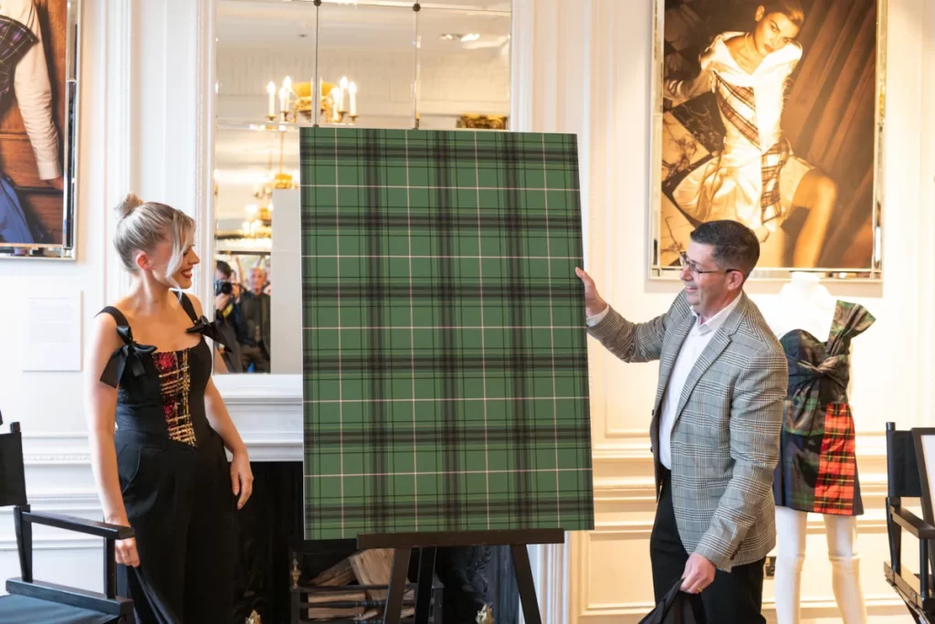 Scottish designer Siobhan Mackenzie speaking into a microphone beside a mannequin wearing a tartan-inspired dress at Blythswood Square Hotel in Glasgow