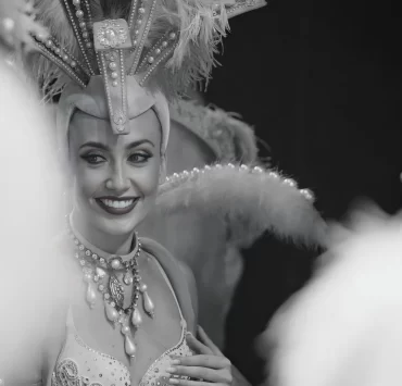 Fallon Robertson smiling in elaborate showgirl costume with feathered headdress, performing as artistic director and choreographer at Trocadero’s, Crossbasket Castle in Scotland.