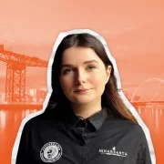 Portrait of Mae MacInnes, general manager of Mharsanta in Glasgow, wearing a branded shirt with an orange-toned background featuring the River Clyde, Finnieston Crane and Squinty Bridge.