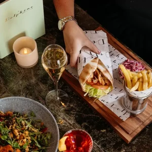 A person reaches for a chicken gyros wrap served with fries, salad and a glass of champagne at The Delphine in Glasgow.