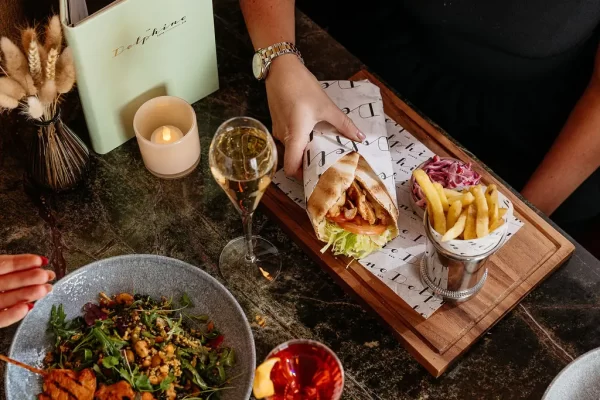 A person reaches for a chicken gyros wrap served with fries, salad and a glass of champagne at The Delphine in Glasgow.