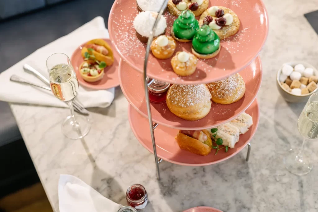 Three-tier stand with festive afternoon tea at Champagne Corner in Glasgow, including sandwiches, scones, sweet treats, and a glass of champagne on a marble table.