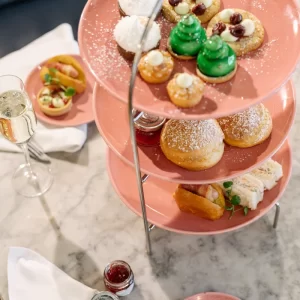 Three-tier stand with festive afternoon tea at Champagne Corner in Glasgow, including sandwiches, scones, sweet treats, and a glass of champagne on a marble table.
