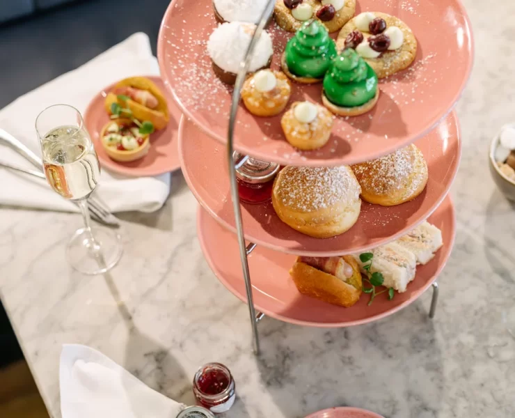 Three-tier stand with festive afternoon tea at Champagne Corner in Glasgow, including sandwiches, scones, sweet treats, and a glass of champagne on a marble table.
