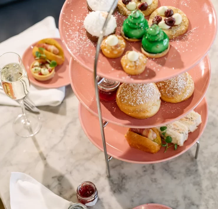 Three-tier stand with festive afternoon tea at Champagne Corner in Glasgow, including sandwiches, scones, sweet treats, and a glass of champagne on a marble table.