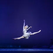 Ballet dancer Constance Devernay leaps across the stage as the Snow Queen, surrounded by an icy, winter-themed set.