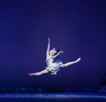 Ballet dancer Constance Devernay leaps across the stage as the Snow Queen, surrounded by an icy, winter-themed set.