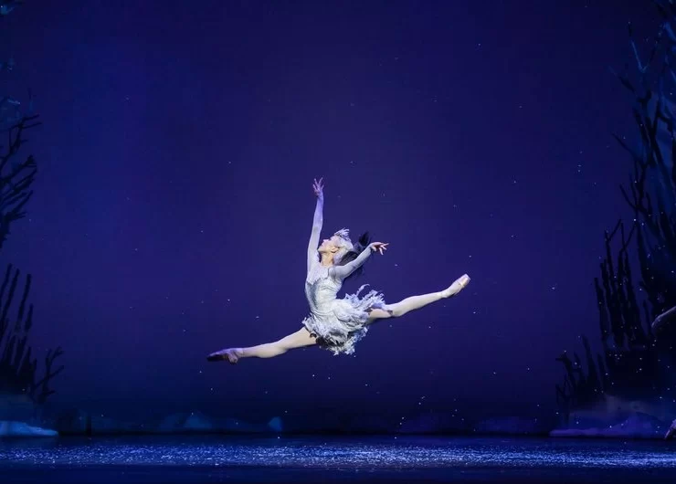 Ballet dancer Constance Devernay leaps across the stage as the Snow Queen, surrounded by an icy, winter-themed set.