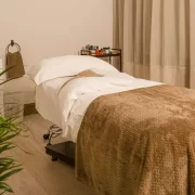Relaxing spa treatment room at The Retreat Glasgow with a massage bed, soft taupe blankets, skincare products and warm, neutral décor.