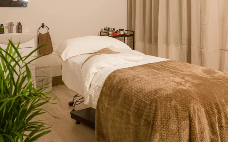 Relaxing spa treatment room at The Retreat Glasgow with a massage bed, soft taupe blankets, skincare products and warm, neutral décor.