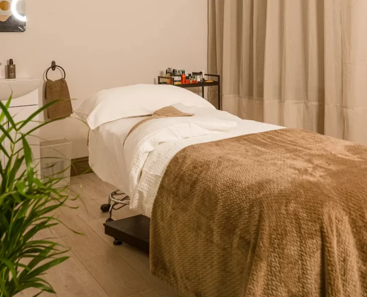 Relaxing spa treatment room at The Retreat Glasgow with a massage bed, soft taupe blankets, skincare products and warm, neutral décor.