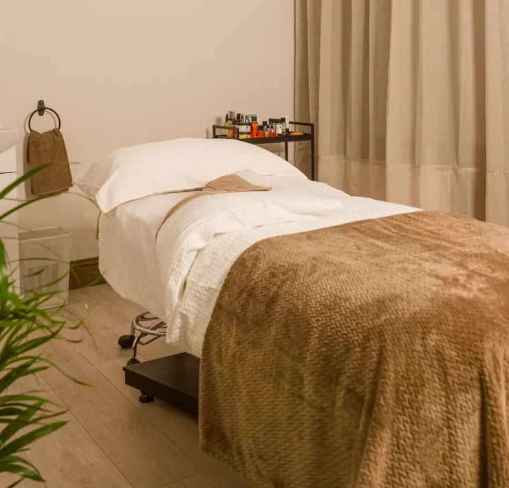 Relaxing spa treatment room at The Retreat Glasgow with a massage bed, soft taupe blankets, skincare products and warm, neutral décor.