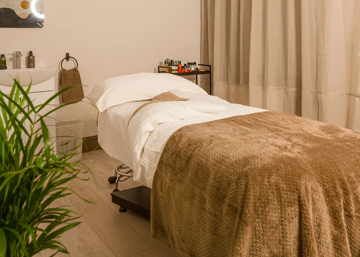Relaxing spa treatment room at The Retreat Glasgow with a massage bed, soft taupe blankets, skincare products and warm, neutral décor.