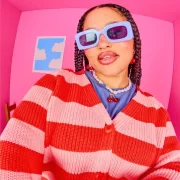 Models wearing colourful Lucy & Yak cardigans, knitwear and graphic outfits in a bright pink studio.