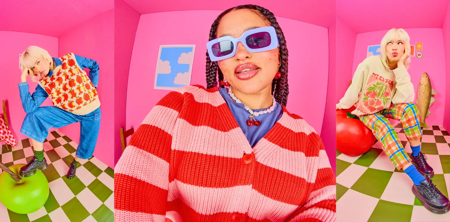 Models wearing colourful Lucy & Yak cardigans, knitwear and graphic outfits in a bright pink studio.